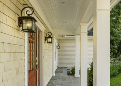 Carolina Electrical Supply Company | lit outdoor sconces by a wooden door leading to a slate tile porch of a white home with shaker siding